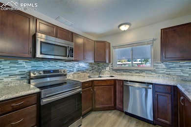 Kitchen featuring stainless steel  appliances with tasteful backsplash, light wood-type flooring, light stone counters, and dark brown cabinets