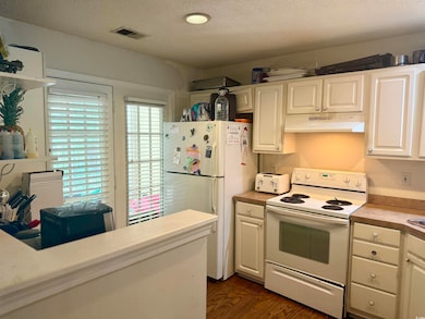 Kitchen with white appliances, under cabinet range hood, light countertops, white cabinetry, and a textured ceiling