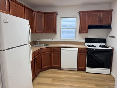 Kitchen featuring white appliances, light wood finished floors, light countertops, under cabinet range hood, and brown cabinetry