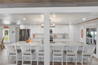 Kitchen with plenty of natural light, white cabinets, backsplash, light stone counters, and recessed lighting