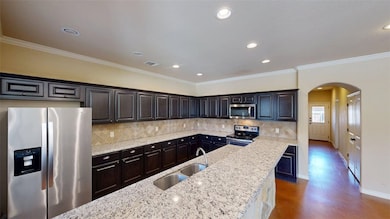 Kitchen featuring appliances with stainless steel finishes, backsplash, recessed lighting, light stone counters, and ornamental molding