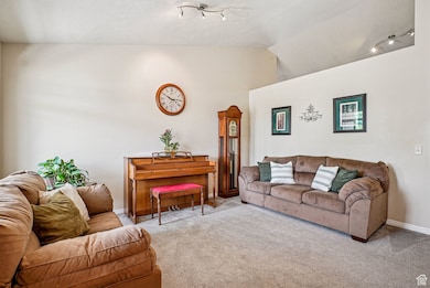 Living room with vaulted ceiling, carpet flooring, and rail lighting