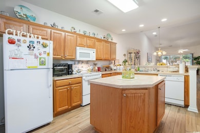 Kitchen with white appliances, a peninsula, light countertops, a kitchen island, and light wood-style floors