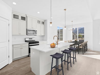 Kitchen featuring stainless steel appliances, a kitchen bar, hanging light fixtures, glass insert cabinets, and an island with sink