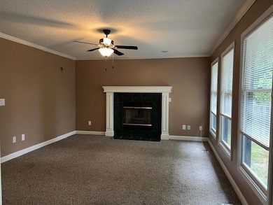 Unfurnished living room featuring a tiled fireplace, a textured ceiling, carpet floors, ornamental molding, and ceiling fan