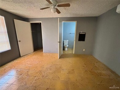 Unfurnished bedroom featuring ceiling fan, a textured ceiling, ensuite bath, and a closet