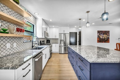 Kitchen with white cabinetry, dark stone counters, stainless steel appliances, open shelves, and hanging light fixtures