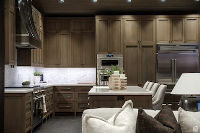Kitchen with high quality appliances, wall chimney range hood, recessed lighting, light countertops, and backsplash