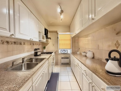 Kitchen with light tile patterned floors, radiator heating unit, white cabinetry, white appliances, and wall chimney range hood