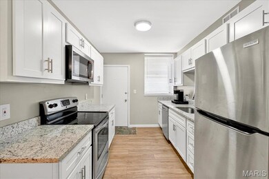 Kitchen with stainless steel appliances, white cabinets, light stone counters, and light wood-style floors