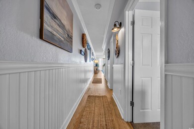 Hall featuring a textured wall, wainscoting, wood finished floors, crown molding, and a decorative wall
