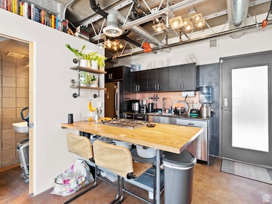 Kitchen with wood counters, a kitchen breakfast bar, stainless steel appliances, concrete flooring, and dark cabinetry