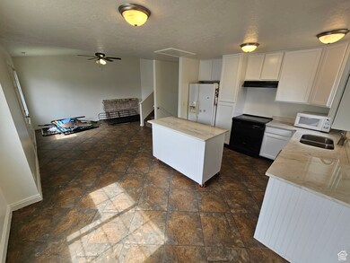 Kitchen with white cabinets, a kitchen island, white appliances, light stone countertops, and a textured ceiling