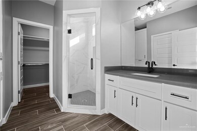 Full bathroom with wood finish floors, a walk in closet, vanity, a marble finish shower, and baseboards