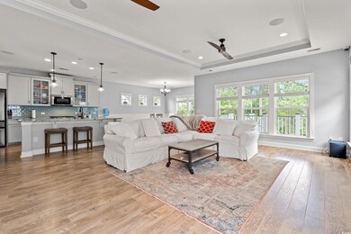 Living room with ceiling fan, light wood-type flooring, a tray ceiling, recessed lighting, and a chandelier