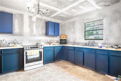 Kitchen with blue cabinets, electric range, light countertops, and a chandelier