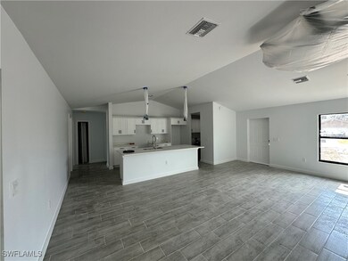 Kitchen with a sink, visible vents, white cabinetry, open floor plan, and a center island with sink