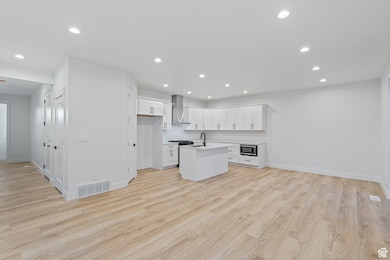 Kitchen featuring white cabinetry, open floor plan, a center island with sink, recessed lighting, and light wood-style floors
