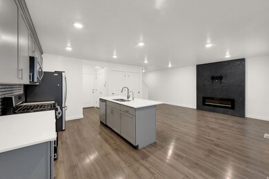 Kitchen with gray cabinetry, stainless steel appliances, dark wood finished floors, an island with sink, and a fireplace