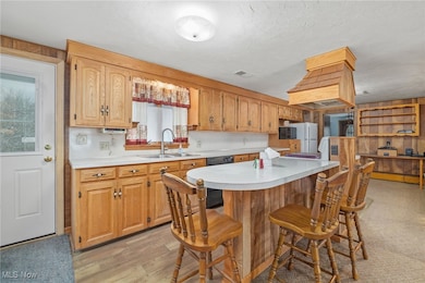 Kitchen with light countertops, a kitchen bar, light wood-type flooring, a textured ceiling, and black appliances