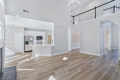 Unfurnished living room featuring a towering ceiling, light wood-type flooring, arched walkways, and a brick fireplace