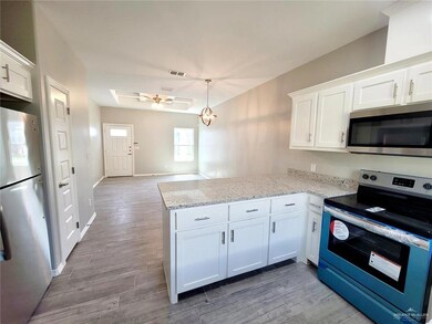 Kitchen with appliances with stainless steel finishes, a peninsula, white cabinetry, and light wood-style floors