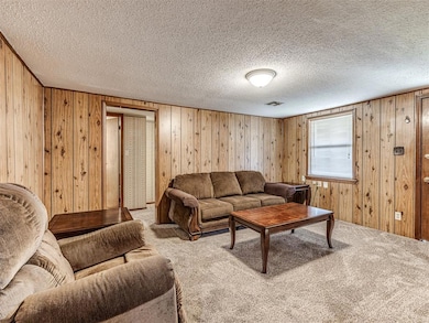 Living room with carpet floors, wooden walls, and a textured ceiling