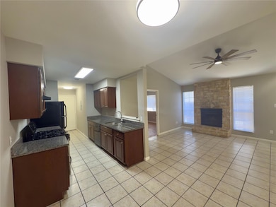 Kitchen featuring light tile patterned flooring, a stone fireplace, ceiling fan, dark stone counters, and vaulted ceiling