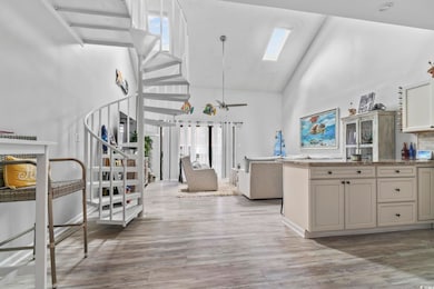Kitchen featuring high vaulted ceiling, a skylight, light stone counters, light wood-style flooring, and open floor plan