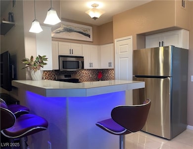 Kitchen with a kitchen bar, stainless steel appliances, white cabinetry, decorative backsplash, and pendant lighting