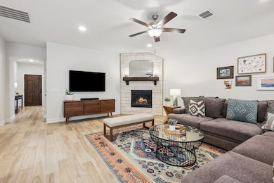 Living room featuring light wood look tile floors, ceiling fan, and an Austin stone fireplace with solid wood mantel