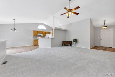 Unfurnished living room featuring vaulted ceiling, light colored carpet, a ceiling fan, and a chandelier