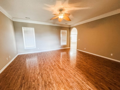 Empty room featuring arched walkways, wood finished floors, ceiling fan, baseboards, and crown molding