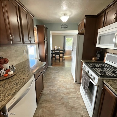 Kitchen featuring white appliances, dark brown cabinets, dark stone countertops, decorative backsplash, and a textured ceiling