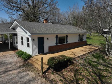 View of front facade featuring a chimney, roof with shingles, and a carport