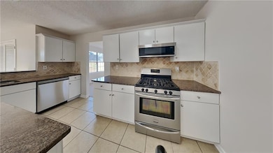 Kitchen featuring appliances with stainless steel finishes, white cabinets, light tile patterned flooring, and a textured ceiling