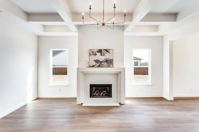 Unfurnished living room featuring beam ceiling, coffered ceiling, light wood-style floors, a fireplace, and a chandelier
