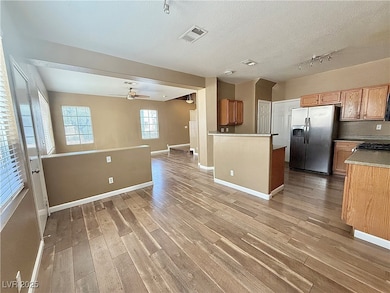 Kitchen featuring open floor plan, brown cabinets, stainless steel fridge, a textured ceiling, and light wood-style flooring