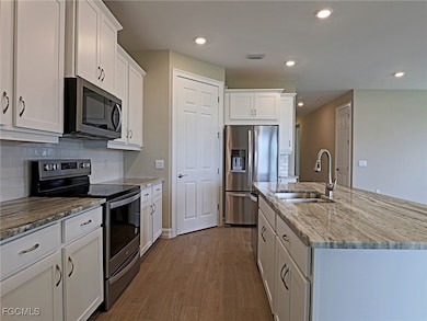 Kitchen featuring stainless steel appliances, an island with sink, dark wood-style flooring, white cabinetry, and recessed lighting