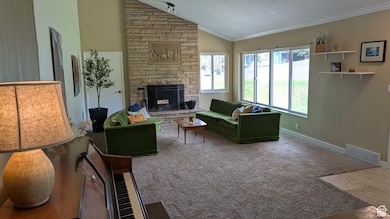 Living area with lofted ceiling, a stone fireplace, carpet flooring, and crown molding