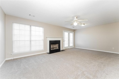 Unfurnished living room featuring light carpet, a fireplace with flush hearth, and a ceiling fan