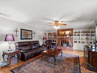 Living area with light wood finished floors, ceiling fan, a textured ceiling, crown molding, and a fireplace
