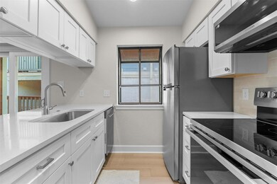 Kitchen with appliances with stainless steel finishes, white cabinetry, light stone counters, and light wood-style flooring