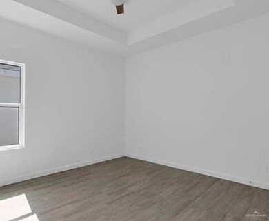 Empty room with a raised ceiling, wood finished floors, and a ceiling fan