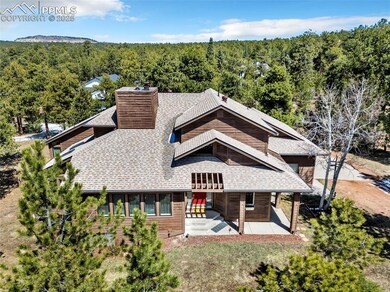 View of front of home featuring a chimney, roof with shingles, a patio area, a balcony, and a wooded view