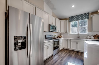 Kitchen with white cabinetry, appliances with stai