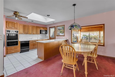 Kitchen with a skylight, a peninsula, light tile patterned floors, tasteful backsplash, and light colored carpet