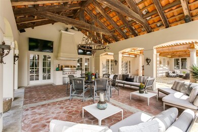 Another view of the spacious covered patio with grilling station, two television, wood beamed ceiling with trusses and more.