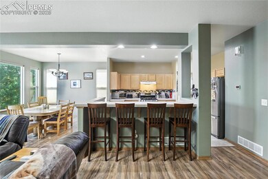 Kitchen featuring light brown cabinetry, stainless steel appliances, wood finished floors, a kitchen breakfast bar, and a chandelier