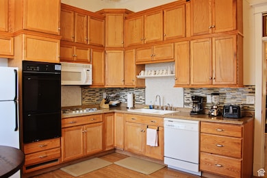 Kitchen with white appliances, decorative backsplash, light wood finished floors, brown cabinets, and ornamental molding